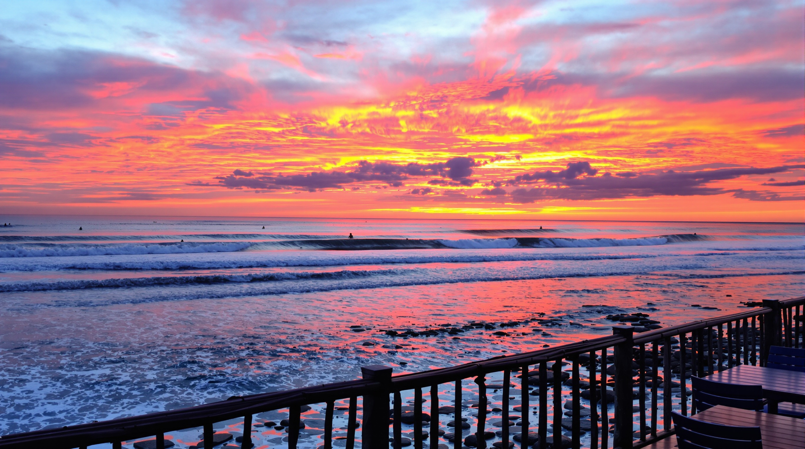 Coucher de soleil spectaculaire vu depuis une terrasse aux Almadies avec silhouettes de surfeurs sur les vagues.