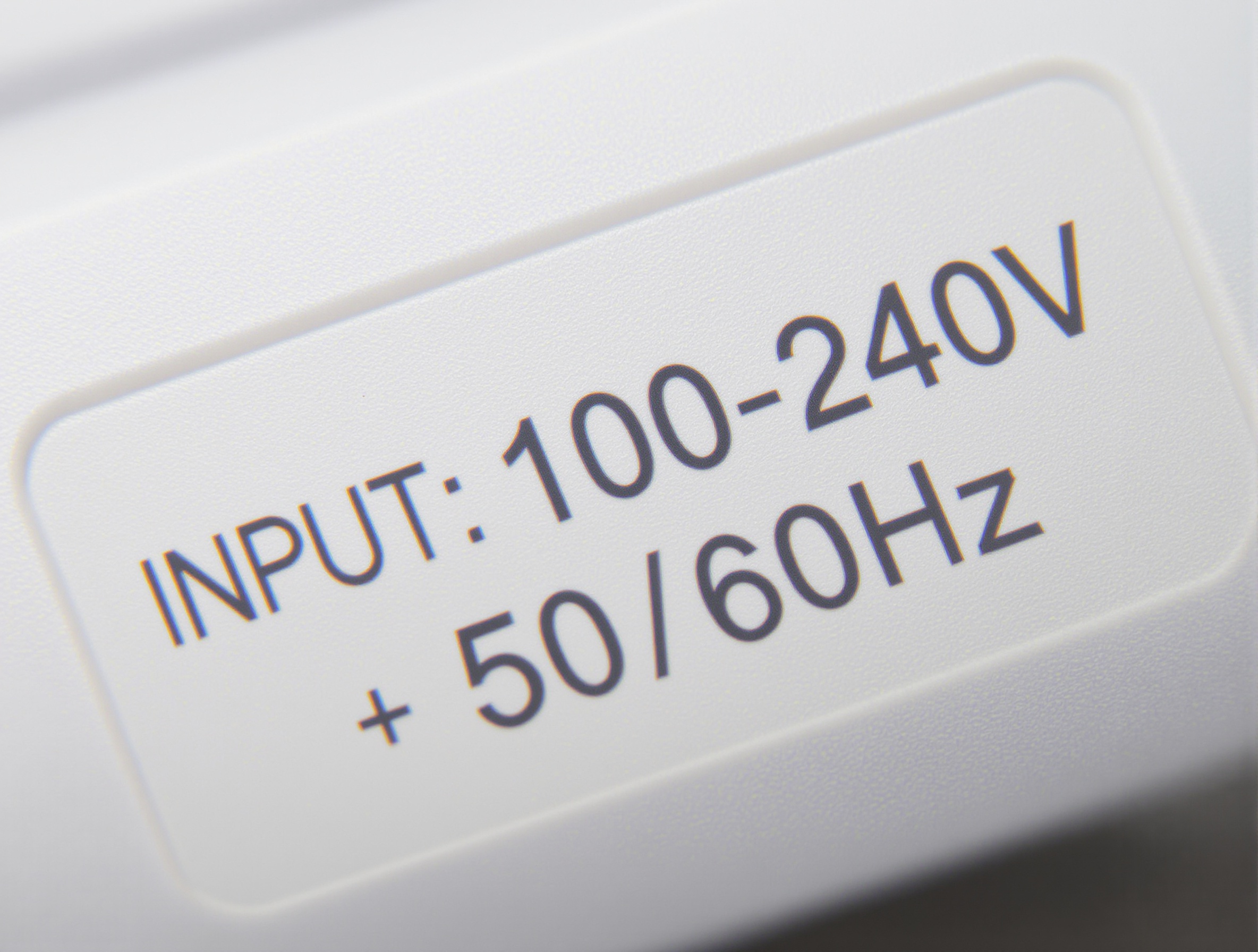 Gros plan sur l'étiquette d'un chargeur d'ordinateur portable, où l'on voit clairement la mention 'INPUT: 100-240V ~ 50/60Hz', illustrant la compatibilité mondiale de l'appareil avec le courant en Inde.