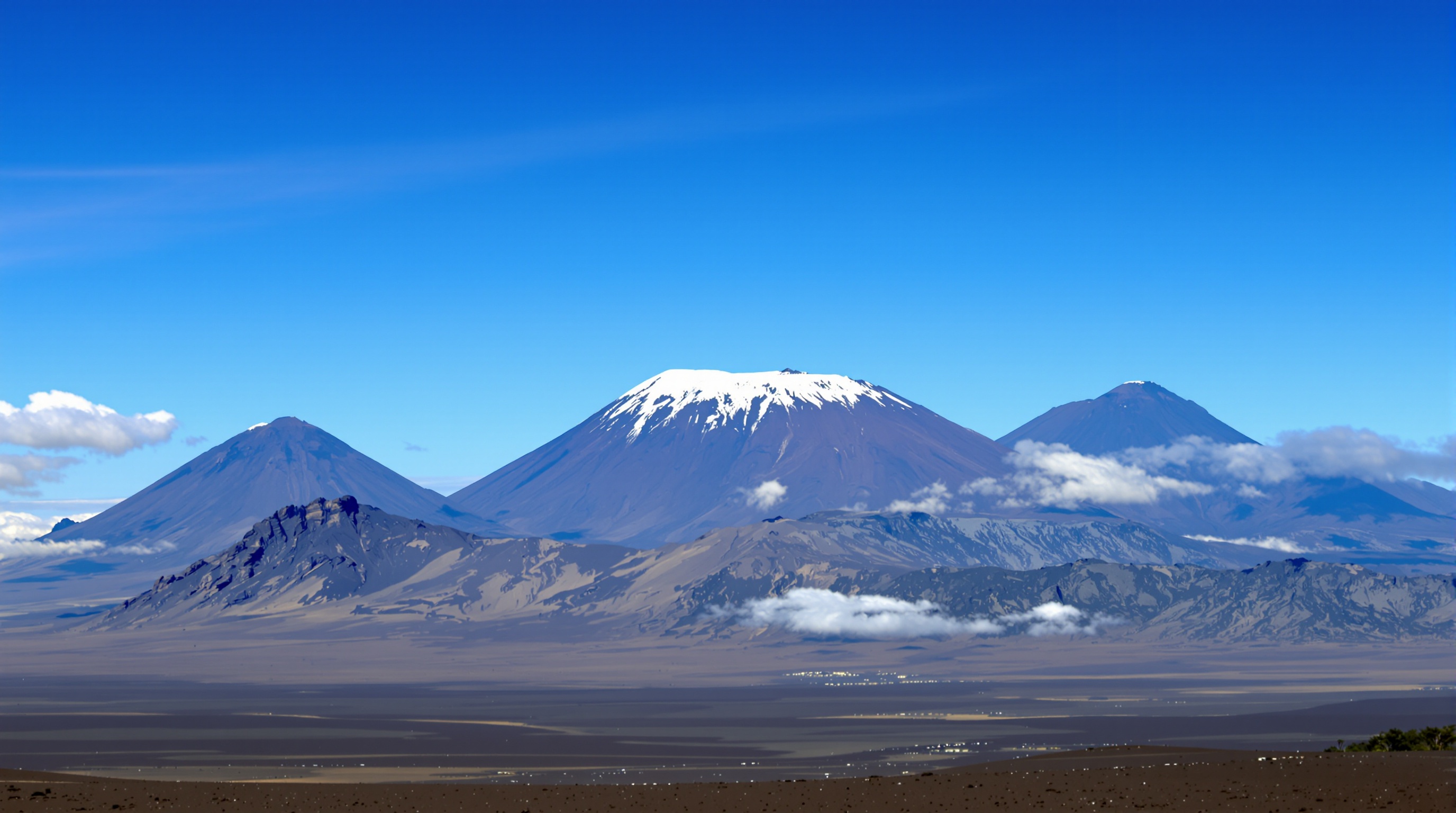 Vue panoramique impressionnante des trois cônes volcaniques du Kilimandjaro : Shira, Mawenzi et Kibo, avec ce dernier coiffé de ses neiges éternelles.